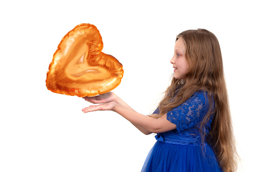 A little girl with long hair in a festive blue dress holds a golden heart-shaped balloon.