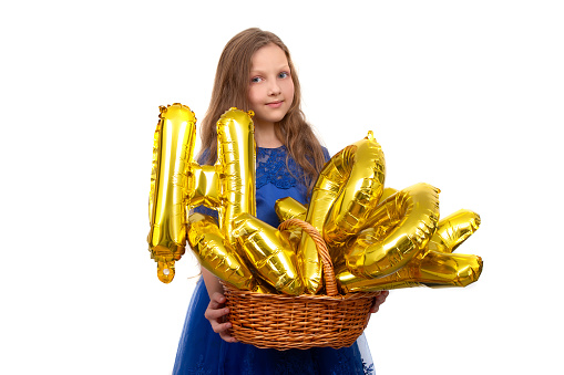 Little girl in a festive blue dress holds a golden set of happy birthday inflatable letters. Isolated on a white background.
