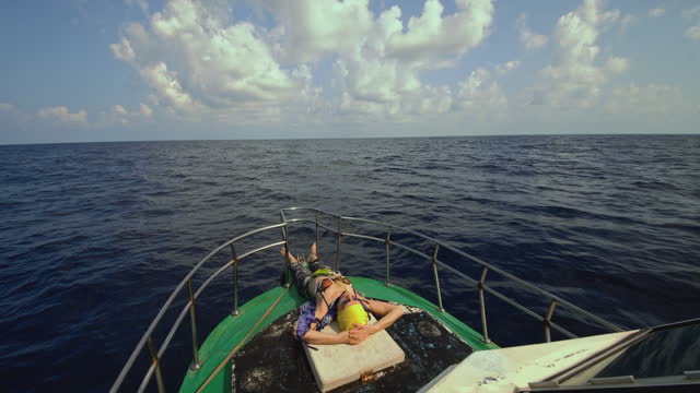A 50-years-old active European woman, a tourist, is lying down, resting, and sunbathing on the deck of a small fishing boat in front of the deckhouse during the deep sea fishing trip in Sri Lanka.