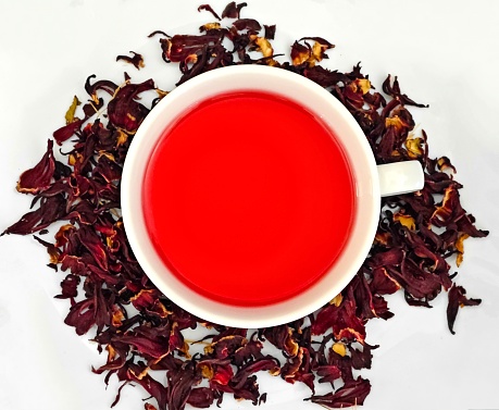 A white cup of red tea with dry petals scattered around it