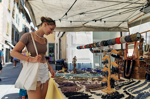 Teenage girl enjoying summer vacations in Ligurian town of Rapallo. \nShe is browsing handmade jewelry on the street stand.\nBeautiful summer day in Rapallo, Catania, Italy.\nShot with Canon R5