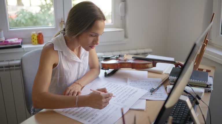 Female violinist practicing playing violin by reading sheet music at home