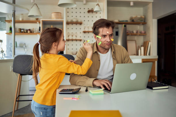 A stressed man using a laptop while babysitting a little girl.