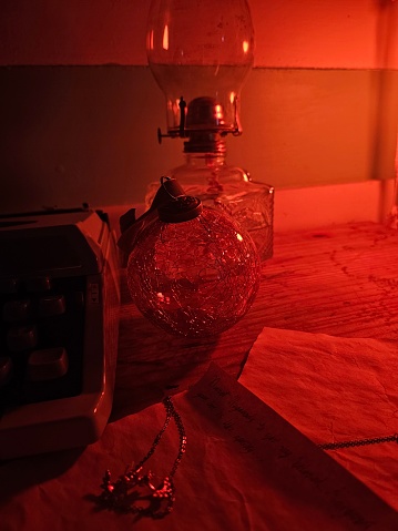 Desktop with typewriter, like lamp, glass ornament, and jewelry in red firelight