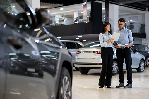 Latin American team of salespersons working together at a car showroom and reading a contract on a tablet