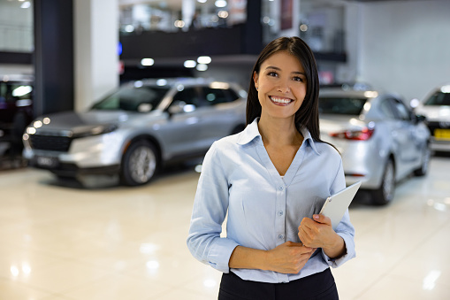 Portrait of a happy Latin American saleswoman working at a car dealership and looking at the camera smiling