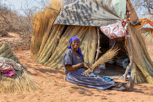 village african woman in front of the shed, manual labor, outdoors in a sunny day in the bush thatch bundle making