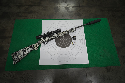 A shooting target and a small caliber rifle with an optical sight in a shooting range on the table. High quality photo