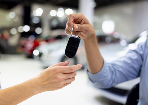 Close-up on a customer receiving the keys of their new car - car ownership concepts