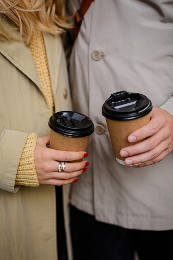 Close-up of hand holding two disposable cups of coffee, woman's and man's hand.