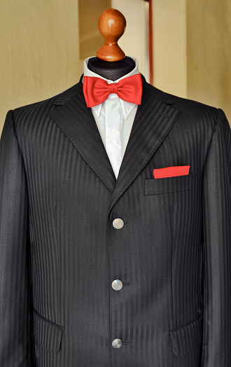A grey striped gentleman's jacket with a white shirt, red bow tie and handkerchief on a taylor's dummy.