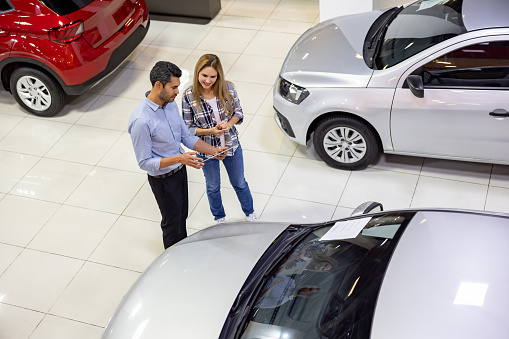 Latin American salesman showing a car to a woman at the dealership - car ownership concepts