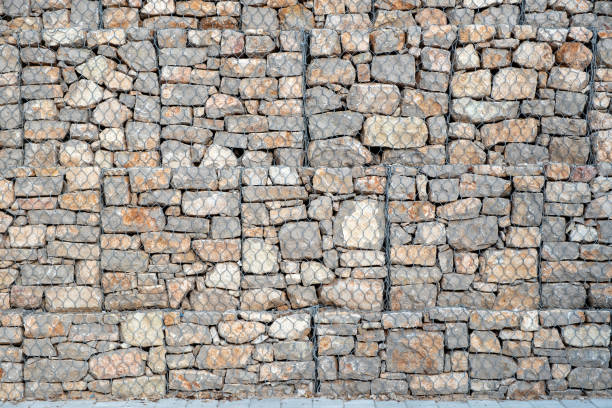 Stonewall behind wire mesh background texture. Metal lattice for protection in front of empty grey rocky wall construction backdrop. Copy space