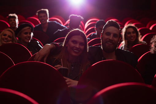 Multiethnic group of happy young people sitting in the cinema and watching movie. Dark tone.