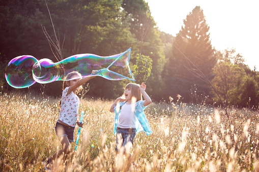 Happy children having fun in grass on sunny summer evening. Kids outdoors in nature blowing bubbles.