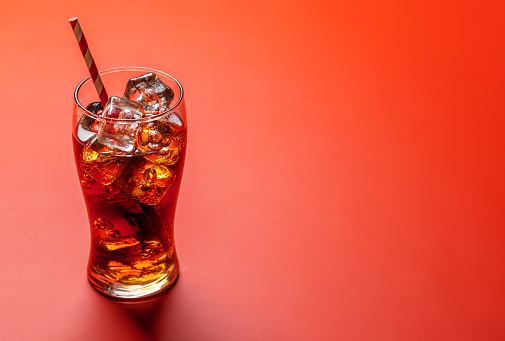 Refreshing glass of cola with ice. Over red background with copy space