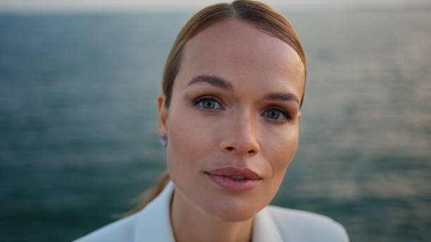 Middle aged model posing near calm ocean surface looking camera confidently close up. Portrait of attractive elegant lady with perfect skin relaxing at evening sea shore. Woman enjoy nature calmness.