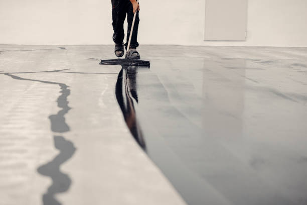 Amazing shot of how epoxy resin is applied. grey coating Worker applies grey epoxy resin to a new floor epoxy floor coating stock pictures, royalty-free photos & images