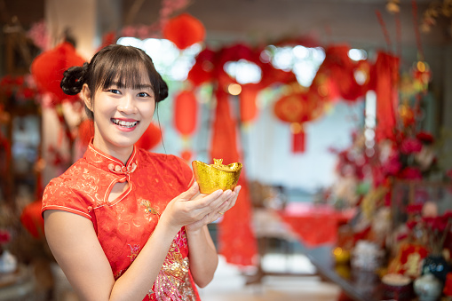 Embrace the festivities as a young Chinese woman, adorned in traditional dress, holds a golden celebration for the auspicious Chinese New Year.