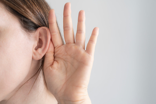 Hand is holding ear of woman to hear better in front of white background.