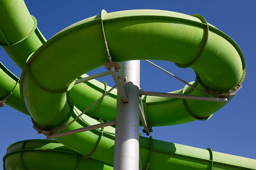 Twisting green water slide in an outdoor water park against the sky, a close up photo of a plastic structure for fun in a turn
