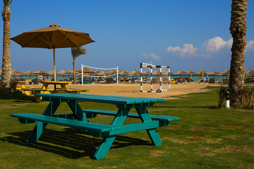Picnic table on the lawn against the backdrop of the beach with a football field and blue sea with a bright clear sky in Egypt