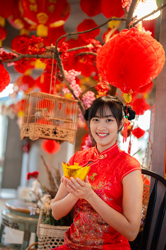 Embrace the festivities as a young Chinese woman, adorned in traditional dress, holds a golden celebration for the auspicious Chinese New Year.