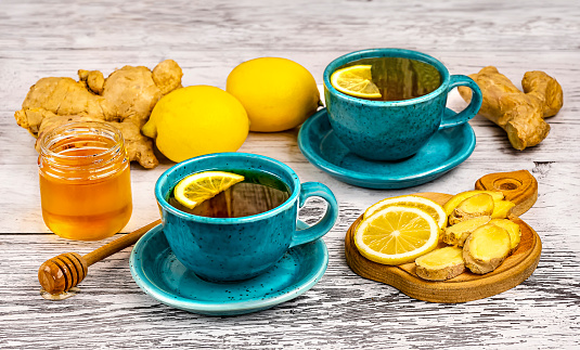 Two blue cups and ingredients for ginger tea, honey, lemons, ginger root on wooden background, side view