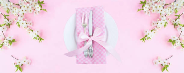 istock White plate, knife, fork and white flowering tree branches on the pink background. Top view. 1977780135