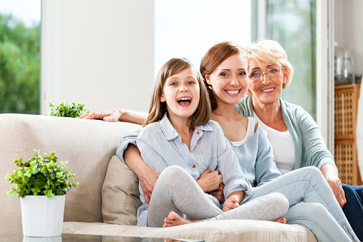 Portrait of a woman and her cute little daughter and mature mother smiling while sitting outside in a back yard at home in summer