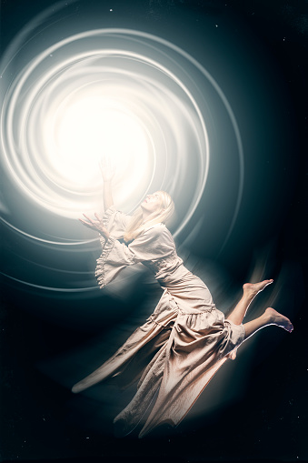 A conceptual image of a woman's spirit drifting to a porthole of light.