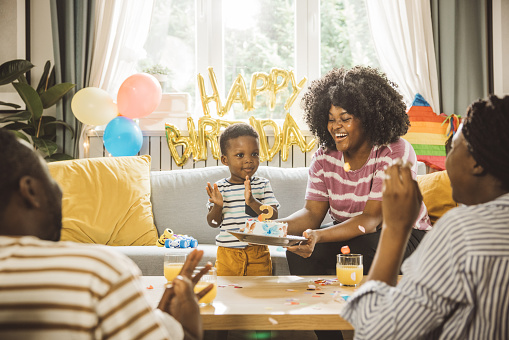 Excited family celebrating little boy's birthday at home. Room is decorated for party and they are happy.