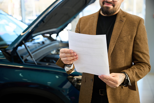 Guy with a beard holds a car purchase agreement in his hands
