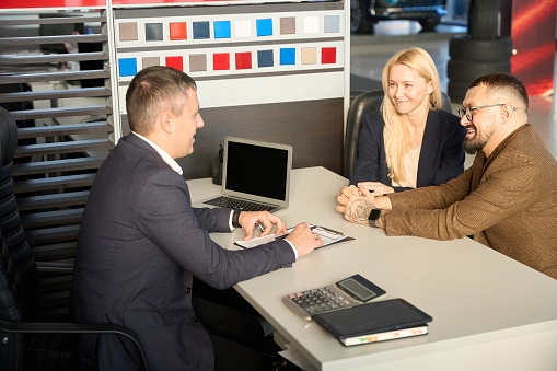 Two buyers and a seller are sitting at a table in front of a car purchase document