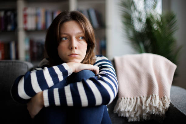 adolescente triste e infeliz abrazando las rodillas, sentada sola en el sofá - hopelessness pensive teenager adolescence fotografías e imágenes de stock