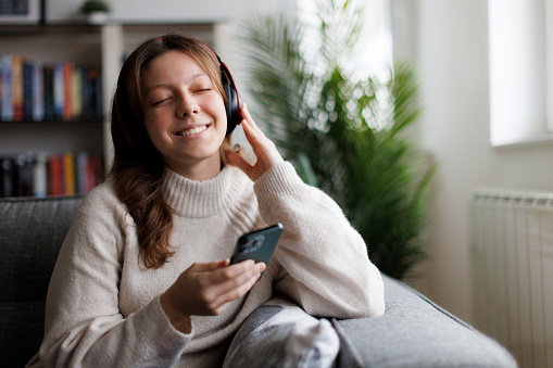 Smiling teenage girl with wireless headphones listening to music at home
