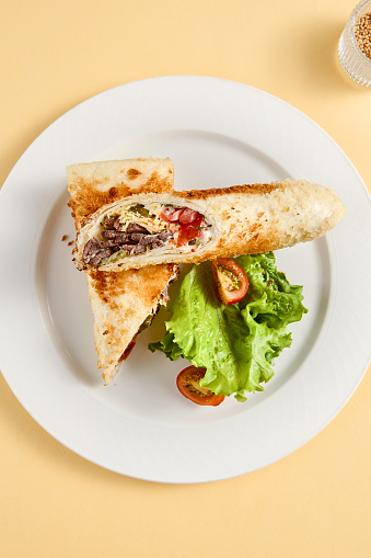 Toasty beef shawarma sandwich with vibrant lettuce and tomato, top view. Ideal for food catalogues and menu design.