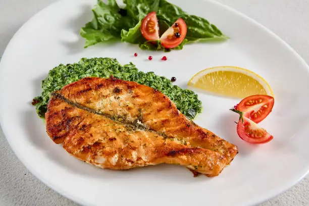 Pan-seared salmon steak with fresh spinach on white plate, perfect for healthy lifestyle and seafood cuisine presentations.