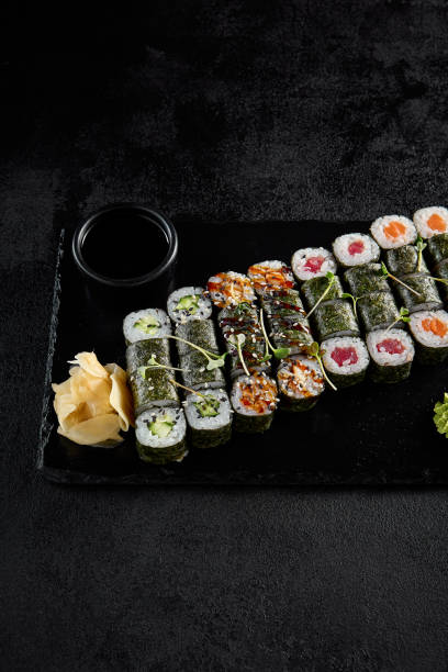 istock Assorted hosomaki sushi set with salmon, tuna, eel, and cucumber on black textured background 1977849794