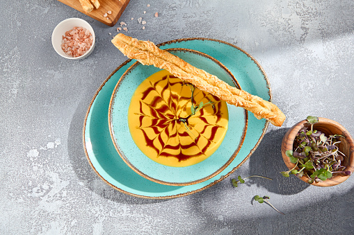 A top-down, horizontal view of a bowl of pumpkin soup with crostini, elegantly presented on a gray concrete table. The minimalist design adds a contemporary flair.