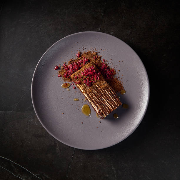 Aesthetic square composition of Medovik honey cake adorned with raspberries, presented on a gray plate against a minimalist black background