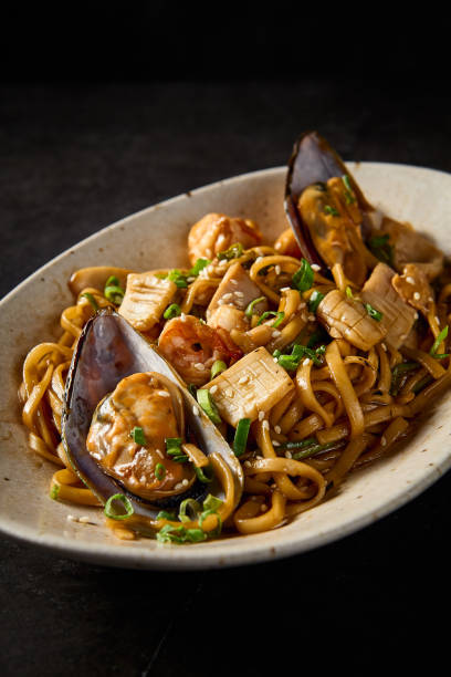 istock A close-up, vertical side shot emphasizing the rich textures of udon pasta with seafood, curated in Asian tradition, on a ceramic plate over a minimalist black tableau 1977851414