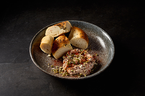 Hummus paired with Uzbek tandoor bread, presented on a dark ceramic plate against a black background; an embodiment of eastern cuisine in a minimalist menu.