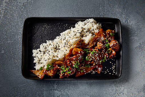 A top-down horizontal perspective of the Kung Pao chicken dish, beautifully presented on a black plate. The rich hues of the sweet-sour sauce complement the gray background.