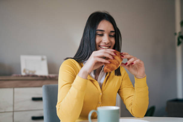 istock Young woman eating croissant at the kitchen 1977862377