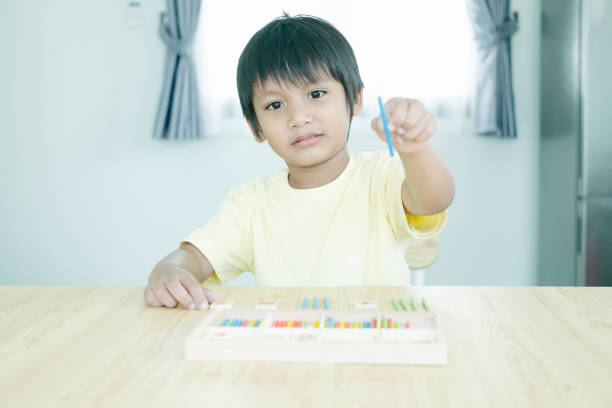 Asian kindergarten kid learn counting and holding mathematic wooden stick.