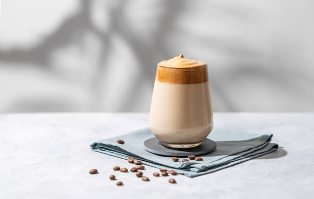 Dalgona coffee. Whipped instant coffee in a glass with beans and shadow on a light background.
