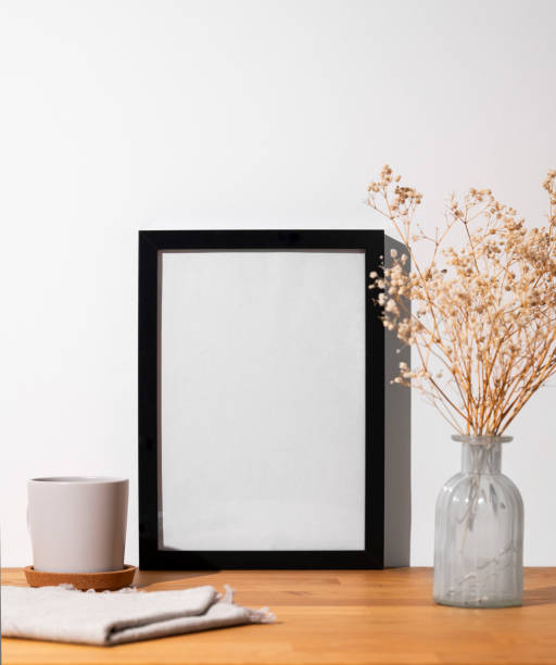istock A  black frame with a blank canvas against a light wall and on a wooden tabletop with vase and cup. 1977903709