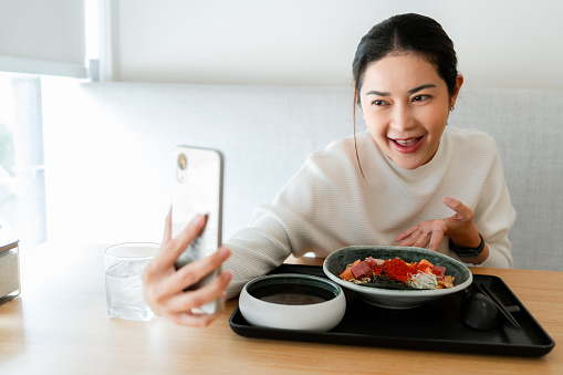 A cheerful woman takes a photo of her meal with a smartphone in Japanese restaurant