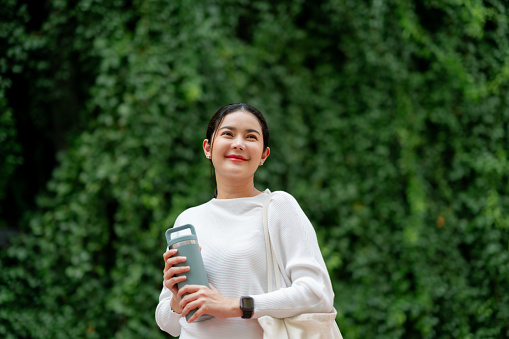 A serene woman with a water bottle enjoys a moment outdoors, with a lush green living wall in the background.